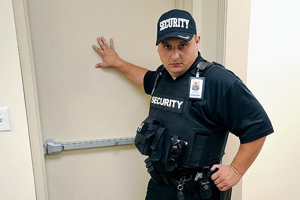 Image of an armed uniformed security job standing by a door.